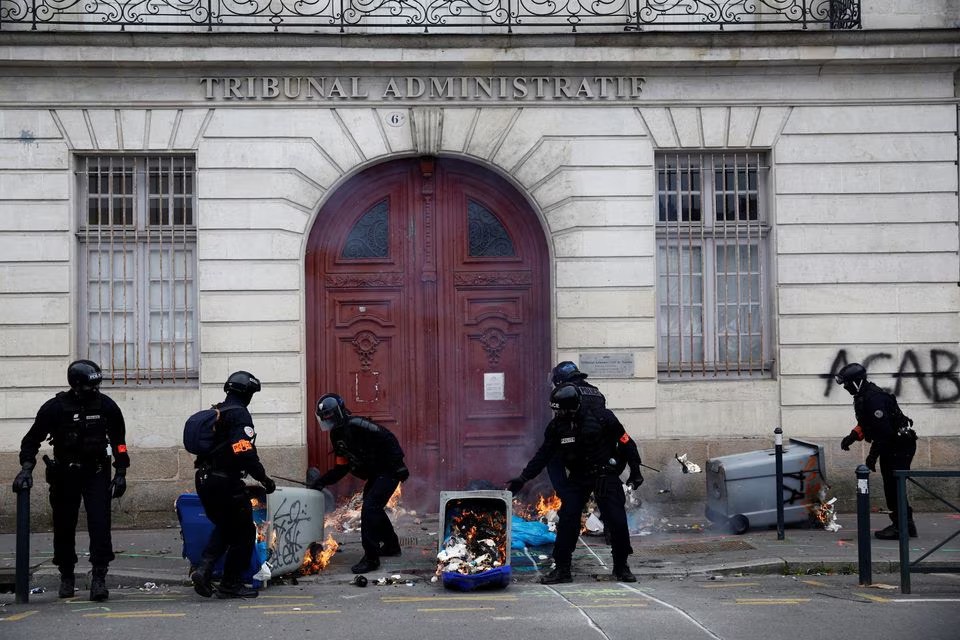 Cảnh s&aacute;t Ph&aacute;p dọn c&aacute;c th&ugrave;ng r&aacute;c đang ch&aacute;y trước lối v&agrave;o t&ograve;a &aacute;n h&agrave;nh ch&iacute;nh tại Paris ng&agrave;y 28/3. Ảnh: Reuters