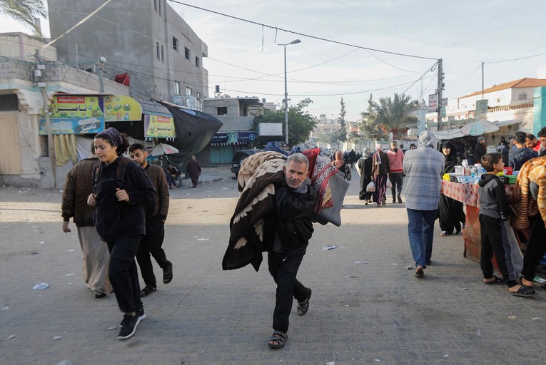 Một người đ&agrave;n &ocirc;ng mang theo đồ đạc, chạy đi sơ t&aacute;n ở Khan Younis, miền nam Gaza, ng&agrave;y 24/11. Ảnh: Reuters